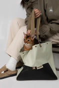 Load image into Gallery viewer, Owner sitting comfortably with the stylish Alpine Olive green cat carrier tote.
